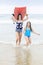 Full length photo of two cute teen girls running on a beautiful beach carrying a bodyboard.