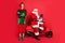 Full length photo of two men elf folded arms santa sit moped hold netbook wear x-mas costume coat cap boots isolated red