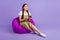 Full length photo of young focused happy woman look empty space play game sit chair  on violet color background