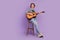 Full length photo of young guy happy positive smile good mood play guitar sitting stool isolated over violet color