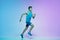 Full length portrait of active young caucasian running, jogging man on gradient studio background in neon light