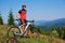 Full length portrait of athletic professional cyclist standing on top of hill