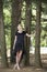 Full length portrait of beautiful barefooted young women wearing black dress while standing under pine tree