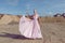 Full length portrait of a blonde high girl in fashionable flying pink maxi dress poses in sand quarry on sunny day.