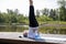 Full-length portrait of a Caucasian elderly woman in yoga vrikshasana poses, tree pose, against the background of a lake