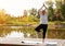 Full-length portrait of a Caucasian elderly woman in yoga vrikshasana poses, tree pose, against the background of a lake