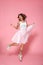 Full length portrait of charming princess with magic wand jumping over pink background