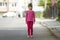 Full length portrait of cute small girl in pink casual clothing and long blond pony tail looking in camera standing on blurred bri