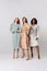 Full-length portrait of diverse beautiful young women in elegant dresses standing together over light background