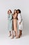 Full-length portrait of diverse beautiful young women in elegant dresses standing together over light background