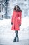 Full-length portrait of ecstatic woman in elegant red coat standing on the street in snowy day. Outdoor photo of fashionable femal