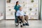 Full length portrait of elderly male patient in wheelchair and his young caregiver at retirement home