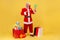 Full length portrait of elderly man with beard wearing santa claus costume surrounded with Christmas presents, pointing at green