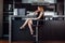 Full-length portrait of elegant woman with fair hair wearing black dress and high heels sitting on a bar chair in