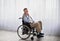 Full length portrait of handicapped senior man in wheelchair feeling desperate and lonely, looking out window indoors