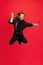 Full-length portrait of liitle boy, kid in image of stylish hairdresser, barber jumping isolated on red background