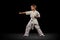 Full-length portrait of little boy, sportsman standing in front stance, high punch pose isolated over black background