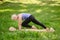 Full-length portrait of a middle-aged woman doing yoga or pilates on a mat in a park in plank pose with knee to hand.