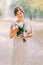 Full length portrait of one beautiful sensual young bride in light white gown and posing at park holding wedding bouquet