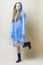 Full Length Portrait of Positive Caucasian Teenager Girl In Blue Dress With Transparent Raincoat and Wellington Boots Against