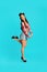 Full length portrait of pretty pinup lady in vintage style outfit lifting leg, being flirty on blue studio background