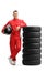 Full length portrait of a racer in a red suit leaning on a pile of tires and holding a helmet