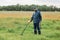 Full length portrait of senior man with metal detector and shovel searching coins or artifacts in green meadow, male enjoying