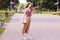 Full length portrait of slender elegant young female walking through recreation zone in native town, wearing hat, red top and