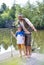 Full length portrait of smiling father and son  standing with fishing  tackles on pier against lake