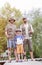 Full length portrait of smiling males standing with fishing rods on pier against trees