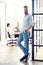 Full length portrait of smiling young man standing in doorway of office. Creative male executive at startup with people