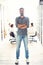 Full length portrait of smiling young man standing in doorway of office. Creative male executive at startup with people