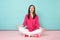 Full length portrait of smiling young woman in rose shirt blouse, white pants sitting on floor isolated on bright pink