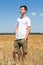 Full length portrait of teen age boy standing on agricultural field with ripe wheat, yellow meadow and blue sky, hands are in