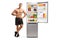 Full length portrait of a topless fitness male model leaning on a fridge and pointing