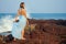 Full length portrait of traveller woman in blue chiffon dress enjoys her tropical beach vacation standing on a rock