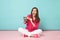 Full length portrait of woman in rose shirt, white pants sitting on floor hold terminal card isolated on bright pink