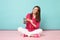 Full length portrait of woman in rose shirt, white pants sitting on floor hold terminal card isolated on bright pink