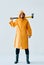 Full length portrait of young handsome man in bright raincoat holding big axe