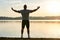 Full-length portrait of young sportsman, wearing grey t-shirt, posing in front of lake at sunset. Muscleman poses, showing muscles