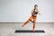 Full length portrait of young sportwoman in black top and orange leggings performs exercises for the muscles of the legs with