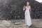 Full length portrait of a young woman in a white wedding dress, looking at camera, posed behind piles of stones