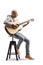 Full length profile shot of a bald man playing an acoustic guitar seated on a chair