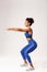 Full length profile shot of determined african-american fitness woman, wearing blue sport outfit, squat with hands