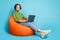 Full length profile side photo of positive girl sit bean chair use laptop enjoy online communication wear green style