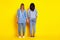 Full length rear photo of two ladies standing hold each other arms isolated on yellow color background
