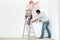 Full-length rear view of couple applying wallpaper to wall