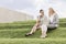 Full length of serious businesswomen looking at laptop while sitting on grass steps against sky