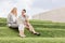 Full length of serious businesswomen looking at laptop while sitting on grass steps against sky