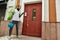 Full length shot of bearded delivery man with thermo backpack using smartphone, standing by the door, while completing